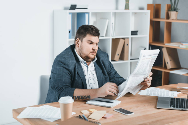 fat businessman in suit reading newspaper at workplace - Fotoğraf, Görsel