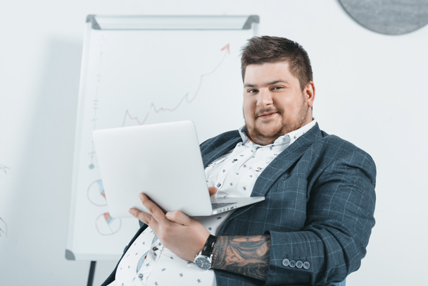 homem de negócios com sobrepeso em terno trabalhando com laptop no escritório
 - Foto, Imagem