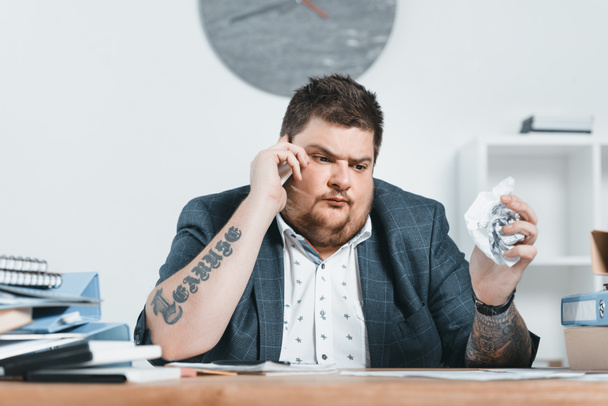 overweight businessman in suit talking on smartphone and working with documents in office - Fotografie, Obrázek