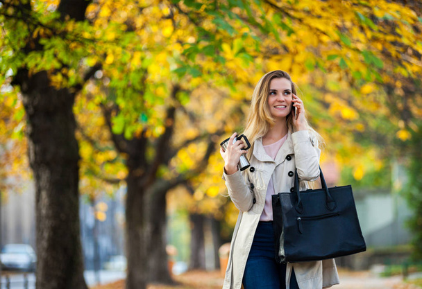 Beautiful woman talking smartphone walking colorful autumn street - Zdjęcie, obraz