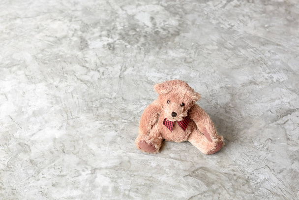 Милая игрушка плюшевого медведя сидит в одиночестве на фоне цементной стены
 - Фото, изображение