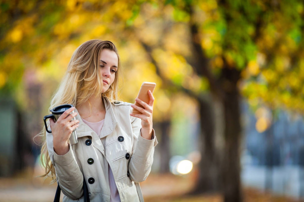 Beautiful woman using smartphone walking colorful autumn street - Zdjęcie, obraz