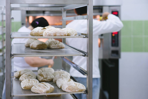 Bäcker überprüft frisch gebackenes Brot in der Küche der Bäckerei - Foto, Bild