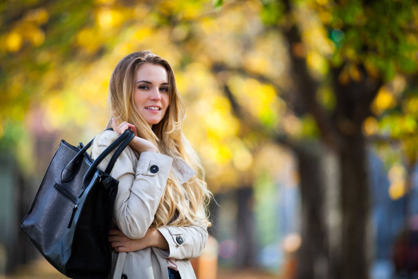 Young woman in coat smiling in the colorful autumn city - 写真・画像