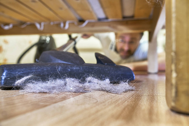Мужчина чистит пол под кроватью пылесосом
 - Фото, изображение