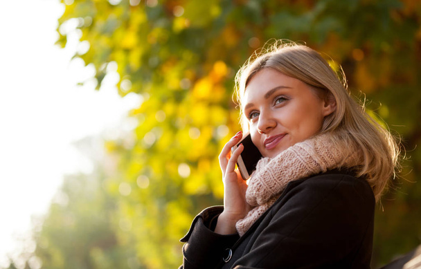 Woman talking on phone outdoor at the street during autumn day - 写真・画像
