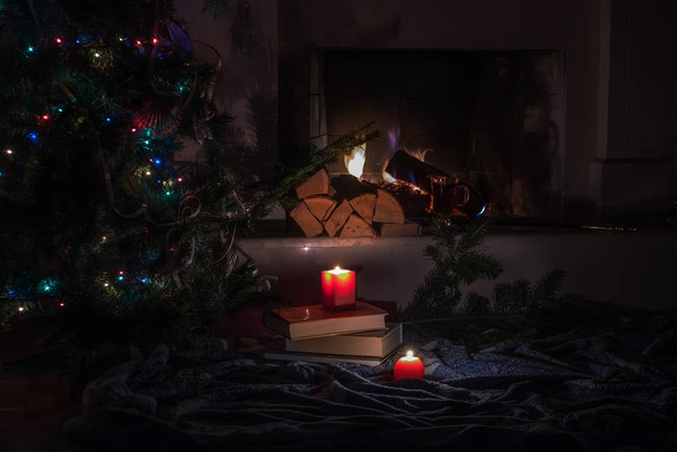 Evening by the fireplace at the Christmas tree, burning candles. Dark photo, cozy home festive atmosphere of relaxation and relaxation. - Photo, Image