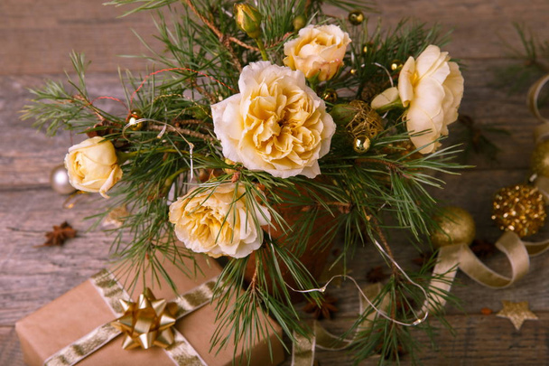 Vánoční dekorace. Dárek, svíčky, světla, zlaté koule na dřevěný rustikální stůl. Složení z borových větví a anglické růže ve váze. - Fotografie, Obrázek
