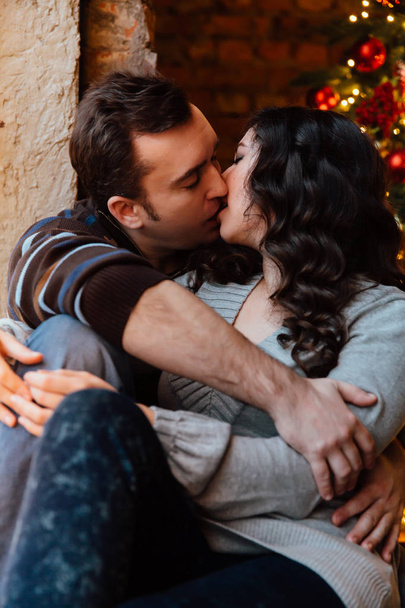 Couple of lovers hugs sitting on the windowsill in the Christmas loft studio. guy is hugging the girl. - Valokuva, kuva