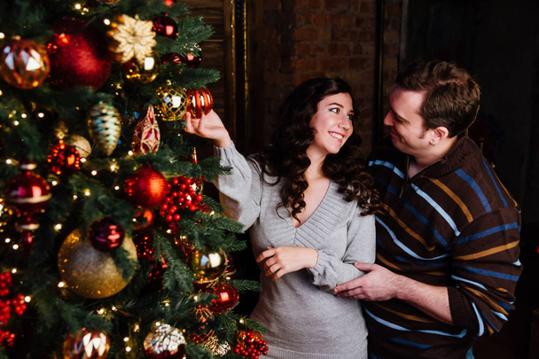 Young couple in love decorates a Christmas tree at home - Foto, afbeelding