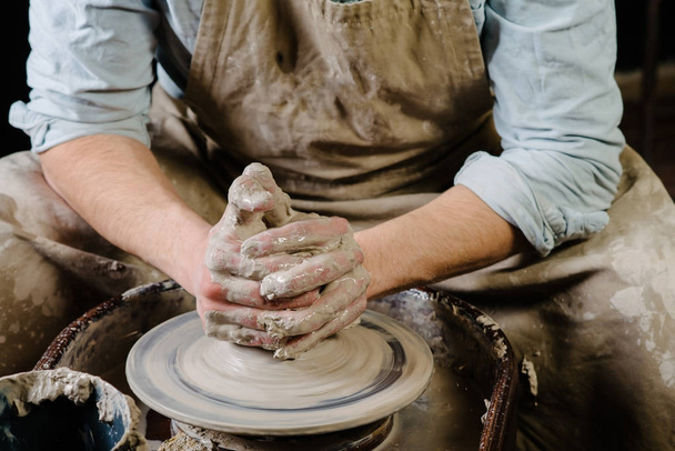 керамика, мастерская, керамика художественная концепция - крупным планом на мужских руках кроется новая посуда с инструментами и водой, мужские пальцы работают с гончарным колесом и сырой фейерверк, вид спереди - Фото, изображение