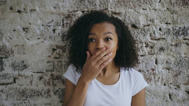 Portrait of curly african american teenager girl actively surprising and wondering on brick wall background - 写真・画像