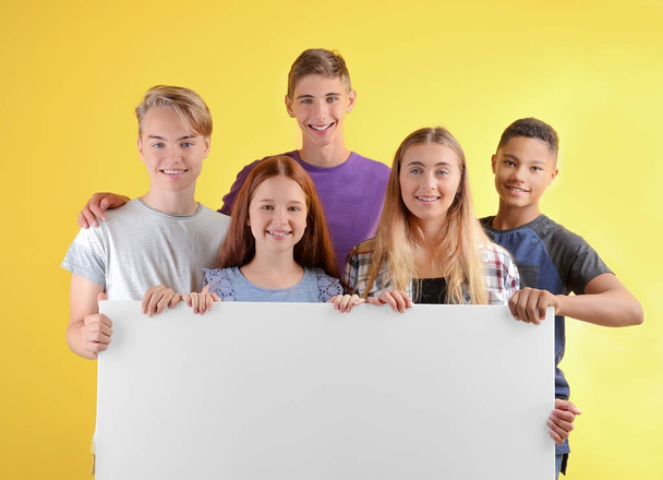 Cute teenagers with blank poster on color background - Фото, зображення