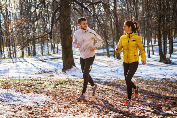 щаслива усміхнена спортивна молода пара біжить в зимовому спортивному одязі, тренування на відкритому повітрі
 - Фото, зображення