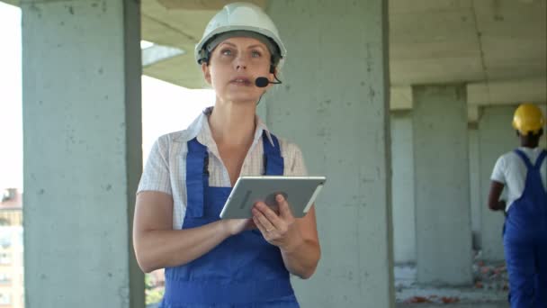 Θηλυκό κατασκευή μηχανικός ανάγνωση σχεδίων χρησιμοποιώντας ψηφιακό tablet και να μιλήσει στους εργαζομένους μέσα από εσωτερικές συνδέσεις - Πλάνα, βίντεο
