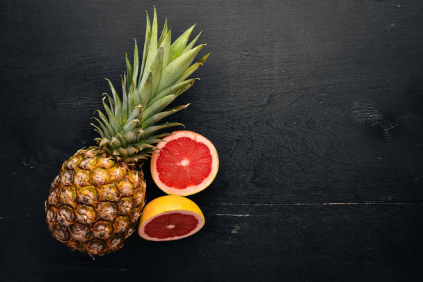 Pineapple and citrus fruits on a wooden background. Tropical fruits and nuts. Top view. Free space for text. - 写真・画像