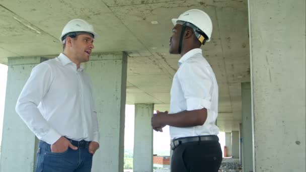 Guapos empresarios de la construcción en cascos y chalecos protectores están estrechando la mano en el sitio de construcción
 - Imágenes, Vídeo