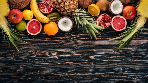Fresh Tropical Fruits. Pineapple, coconut, kiwi, orange, pomegranate, grapefruit. On a wooden background. Top view. Free space for text. - Foto, Bild