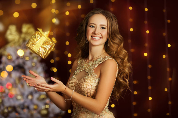 Beautiful young girl is wearing fashion golden dress with gift box - Fotó, kép