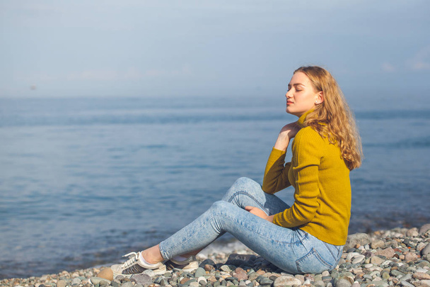 güzel sarışın kız sahilde oturan ve bakarak - Fotoğraf, Görsel
