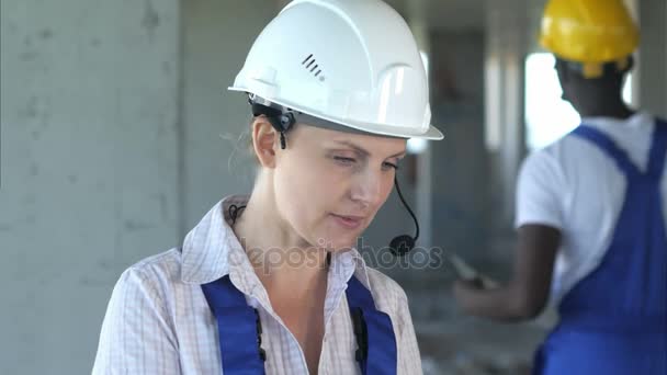 Female construction engineer reading plans and talk to workers through internal links - Footage, Video
