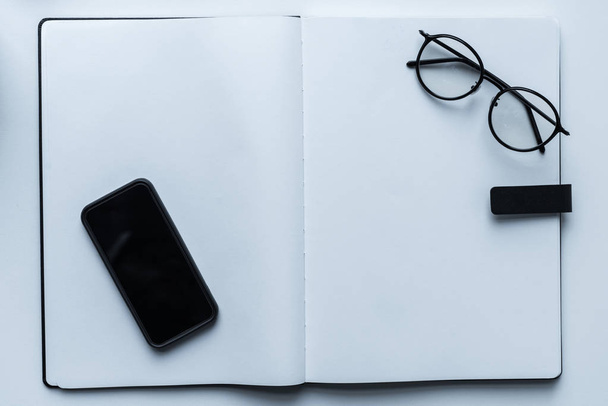 top view of smartphone and glasses on open notebook - Foto, Imagen