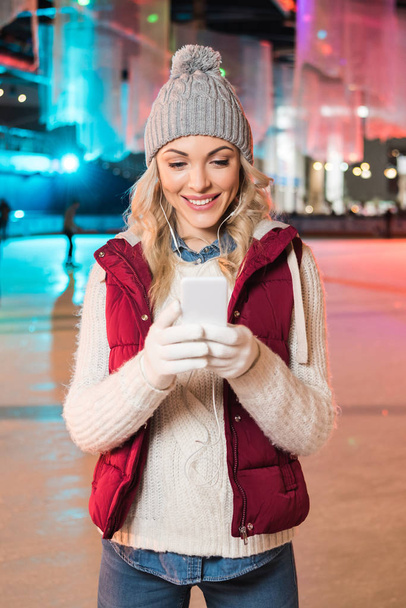 atractiva mujer joven sonriente en auriculares con teléfono inteligente en la pista
  - Foto, Imagen
