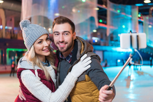 Schönes lächelndes junges Paar macht Selfie mit Smartphone auf Eisbahn - Foto, Bild
