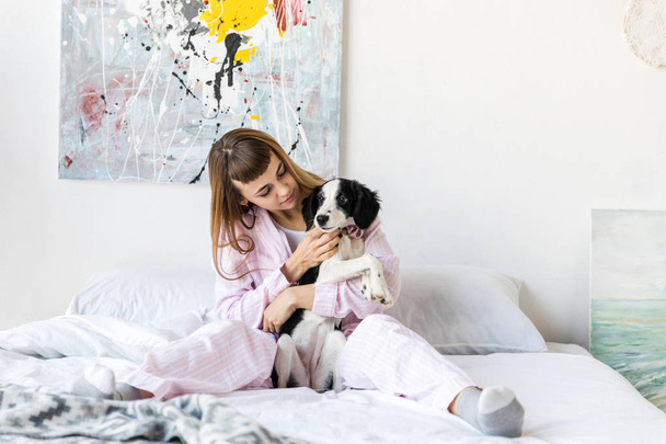 自宅のベッドで休んでいる間子犬を保持しているパジャマを着てはかなりの女性の肖像画 - 写真・画像