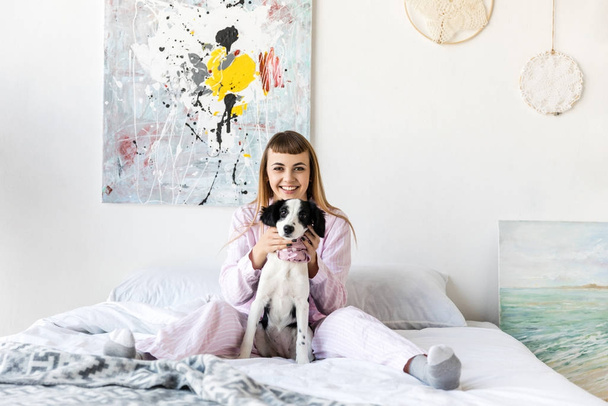 femme heureuse en pyjama et mignon petit chiot reposant sur le lit le matin à la maison
 - Photo, image