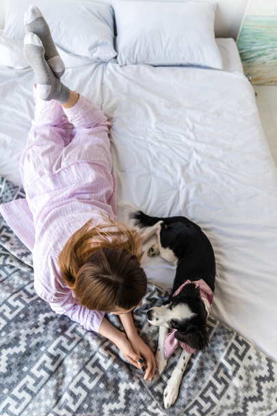 overhead view of woman in pajamas lying on bed together with cute puppy - Foto, Bild