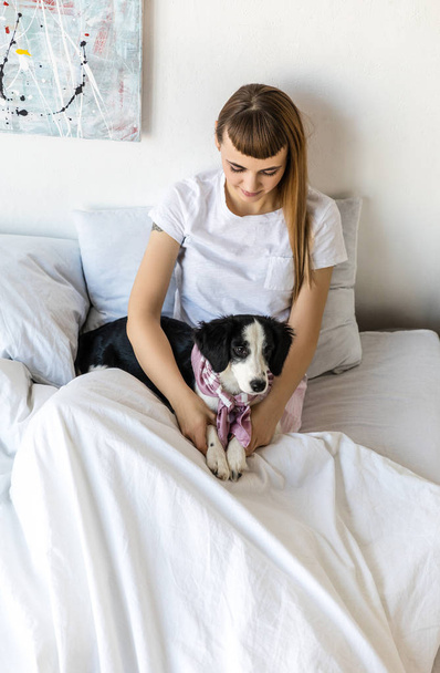 portrait of young woman and cute puppy lying together in bed in morning at home - Foto, immagini