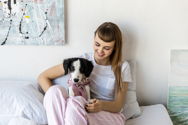 portrait of young woman with little puppy resting in bed in morning at home - Fotó, kép