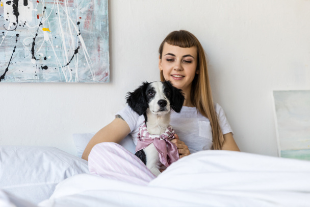 portrait of young woman with little puppy resting in bed in morning at home - Zdjęcie, obraz