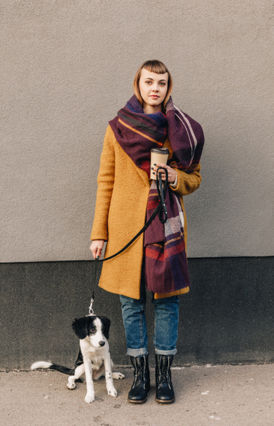 thoughtful woman in stylish jacket with puppy on dog lead standing on street - Zdjęcie, obraz