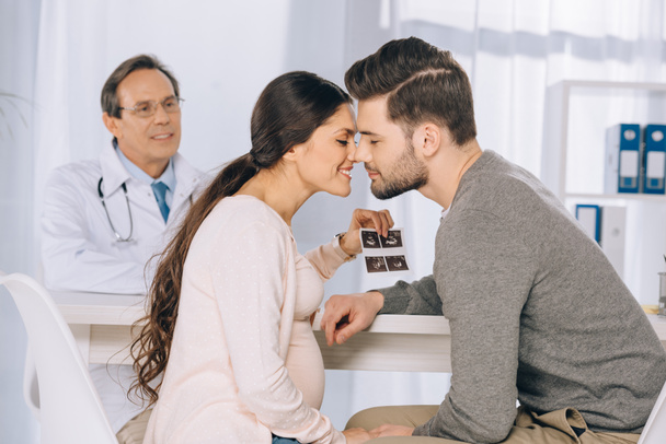 happy couple holding photo of ultrasound diagnostics and kissing - Фото, изображение