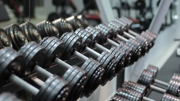 The athlete approaches the shelf with dumbbells and takes one of them and then leaves engaged. A large number of sports equipment. - Footage, Video