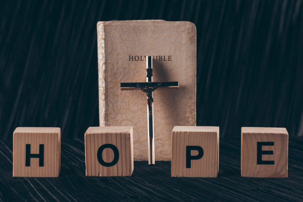 ξύλινα κυβάκια με λέξη ελπίδα και την Αγία Γραφή με σταυρό στον μαύρο πίνακα - Φωτογραφία, εικόνα