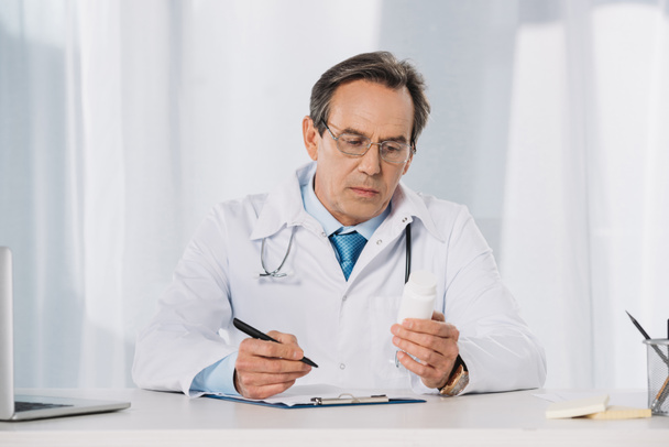 γιατρός εκμετάλλευση στυλό και κοιτάζοντας χάπια - Φωτογραφία, εικόνα
