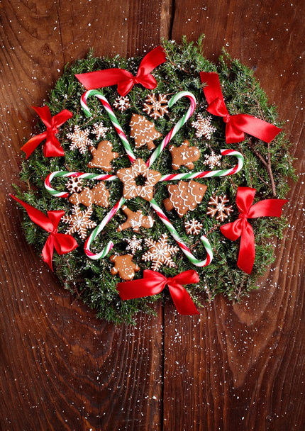 Christmas wreath of fir with ginger cookies,caramel sticks and red ribbon bows.On the wooden background.Snowy.Copy space - Valokuva, kuva