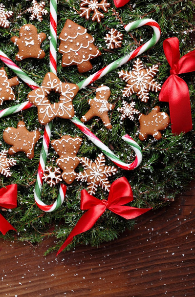 Christmas wreath of fir with ginger cookies,caramel sticks and red ribbon bows.On the wooden background.Snowy.Copy space - Φωτογραφία, εικόνα