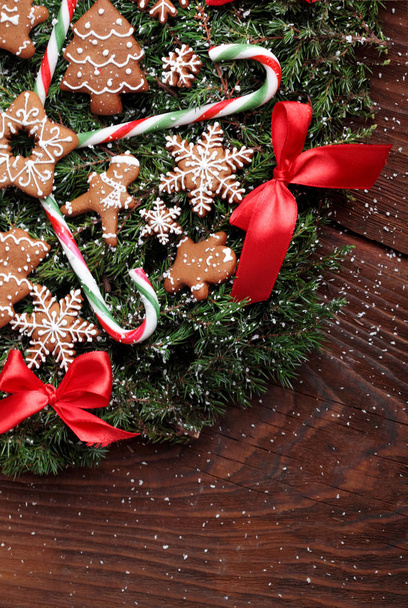 Christmas wreath of fir with ginger cookies,caramel sticks and red ribbon bows.On the wooden background.Snowy.Copy space - Foto, Imagem