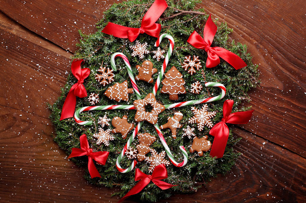Christmas wreath of fir with ginger cookies,caramel sticks and red ribbon bows.On the wooden background.Snowy.Copy space - Foto, Imagem