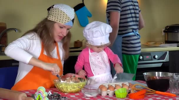 Schattig meisje met hoed van de chef-kok en haar jonge ouders voorbereiding van cookies - Video