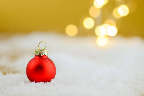 Κόκκινη Χριστουγεννιάτικη μπάλα σε ένα χιόνι σε χρυσό φόντο. - Φωτογραφία, εικόνα