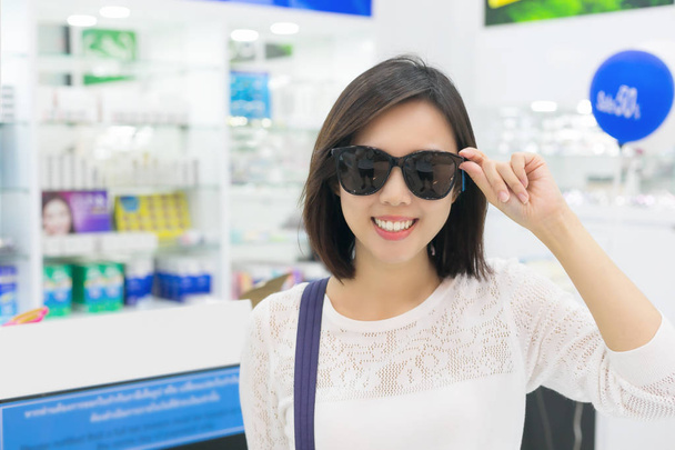 Νεαρή γυναίκα με γυαλιά ηλίου που βλέπουν φωτογραφική μηχανή σε κατάστημα. - Φωτογραφία, εικόνα