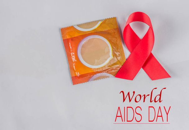 Red AIDS awareness ribbon and condom on white background.  - Φωτογραφία, εικόνα