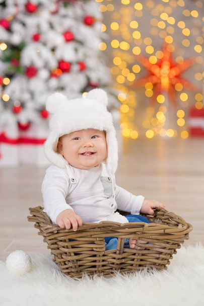 Beautiful little baby boy celebrates Christmas. New Year's holidays. Baby in a Christmas costume casual clothes with gifts on fur close to new year tree in studio decorations. - Фото, зображення