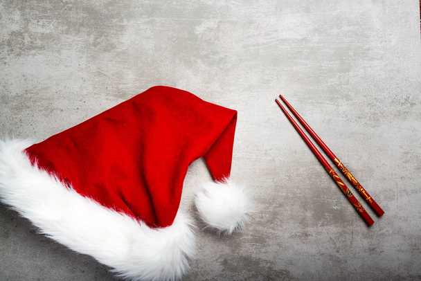 Red santa hat and chopsticks on a gray concrete table - Photo, Image