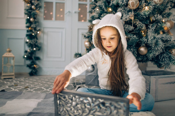 Adorable little girl opening a magical Christmas gift by a Christmas tree - Photo, image
